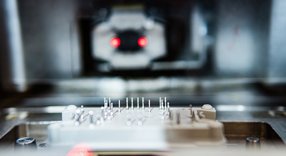 Close-up of a power module with metal pins in a blurry industrial setting, highlighting precision engineering details.