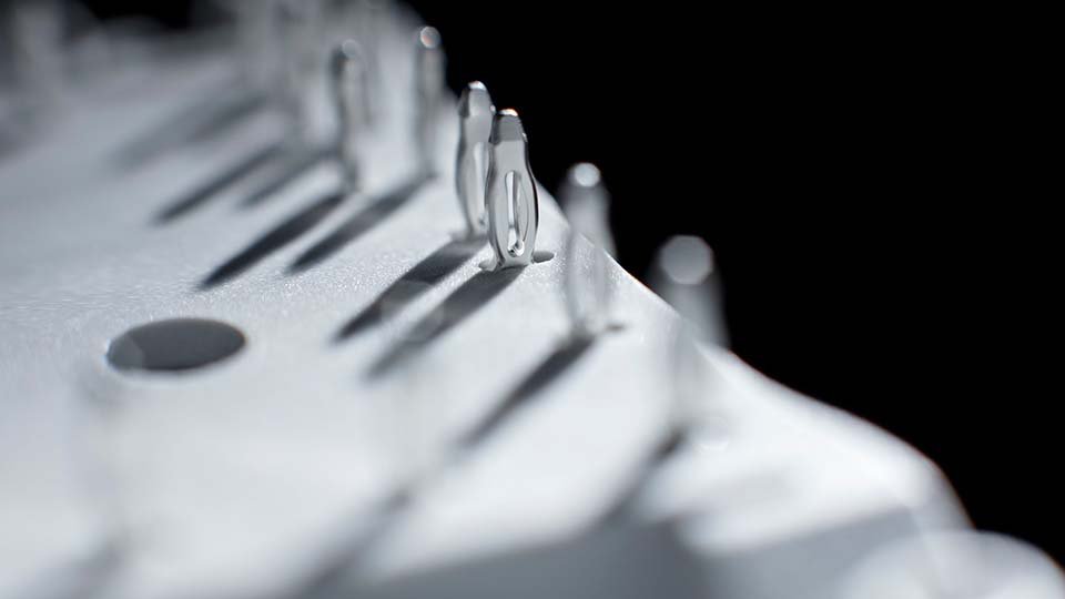 Small metallic figures on a curved surface, casting elongated shadows, with a dark background.