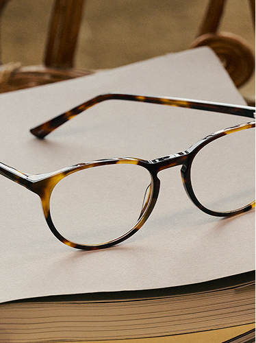 Round tortoiseshell eyeglasses with clear lenses rest on an open book.