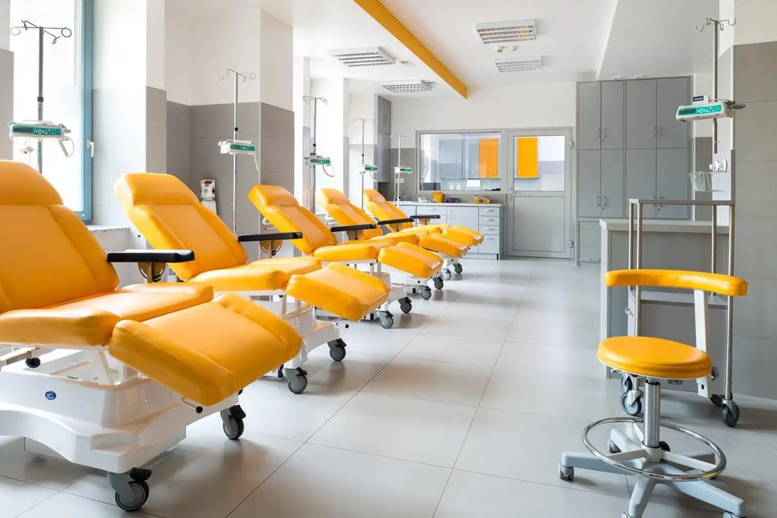 A bright medical treatment room at a Pratia Research site  with rows of yellow reclining chairs and IV stands, designed for patient comfort and care.