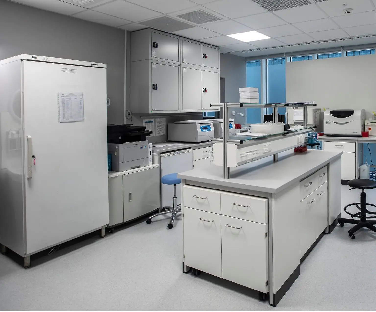 Modern laboratory at a Pratia research site with white cabinets, workstations, and equipment, including a refrigerator, centrifuges, and seating, under bright lighting.