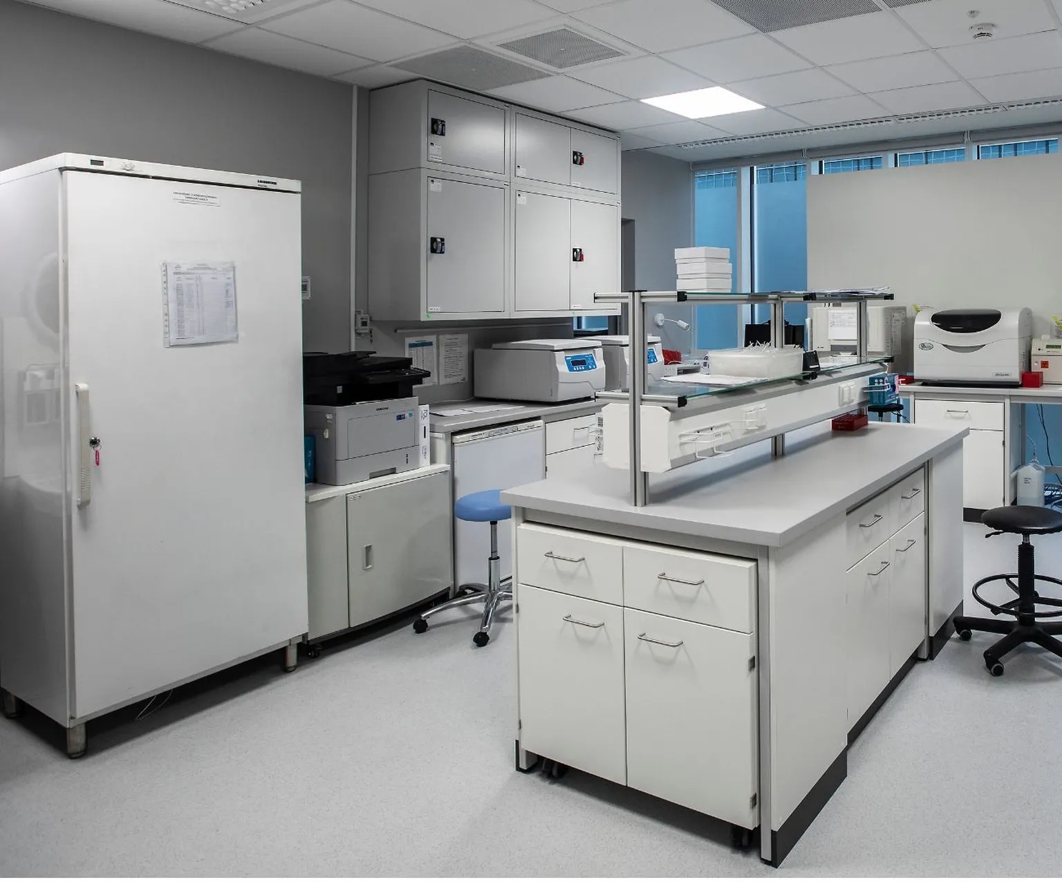 Modern laboratory at a Pratia research site with white cabinets, workstations, and equipment, including a refrigerator, centrifuges, and seating, under bright lighting.