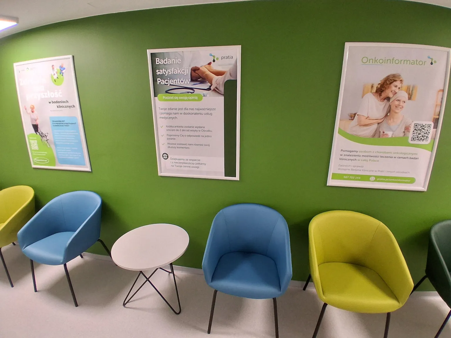A waiting area at  a  Pratia research site in Poland  with colorful chairs, green wall, and three posters promoting medical services and patient satisfaction in Polish.