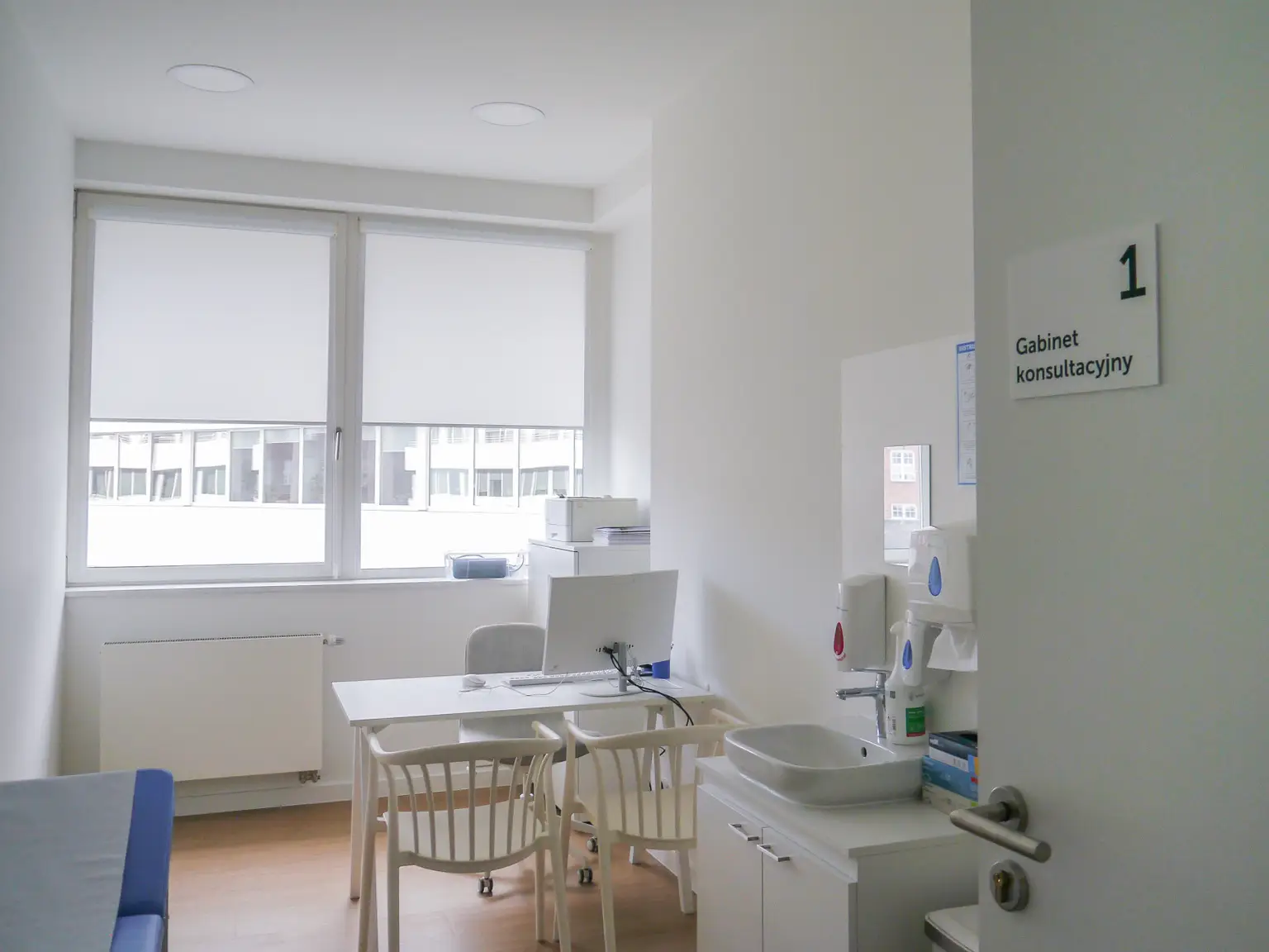 A clean consultation room at Pratia research site with a desk, chairs, computer, and sink. The door has a sign labeled "Gabinet konsultacyjny."