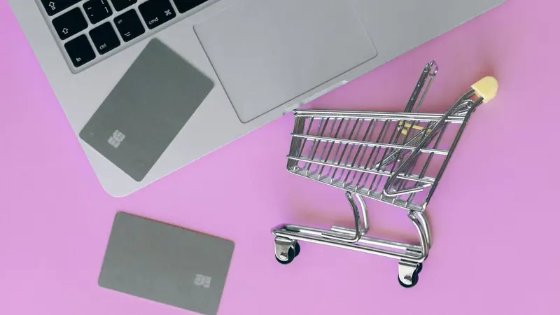 Toy shopping cart beside bank cards on a pink background