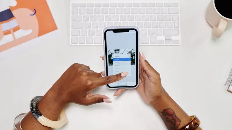 Hands holding a smartphone next to a laptop and coffee