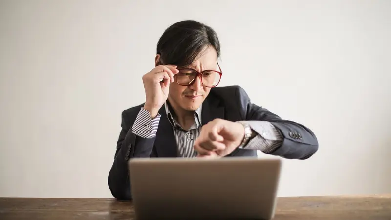Man checking his watch while working at a laptop