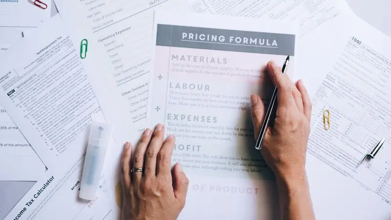 Hands writing on a printed pricing formula sheet