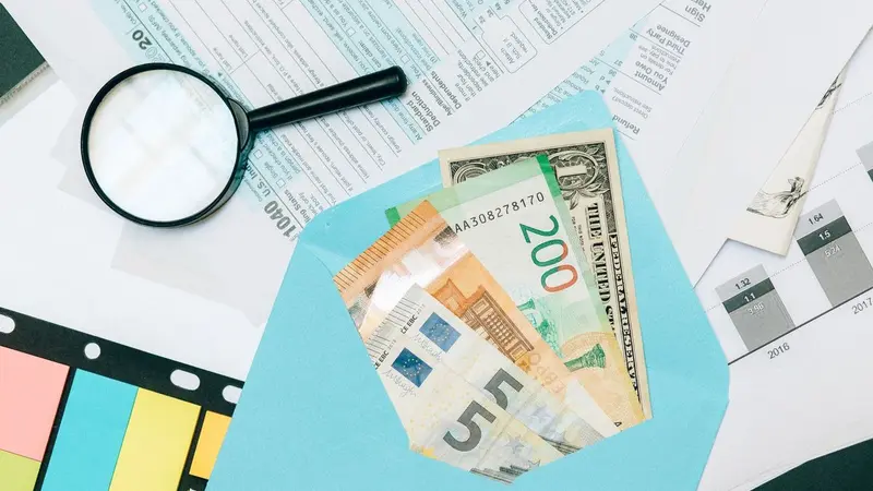 Magnifying glass over banknotes and papers, representing hidden costs