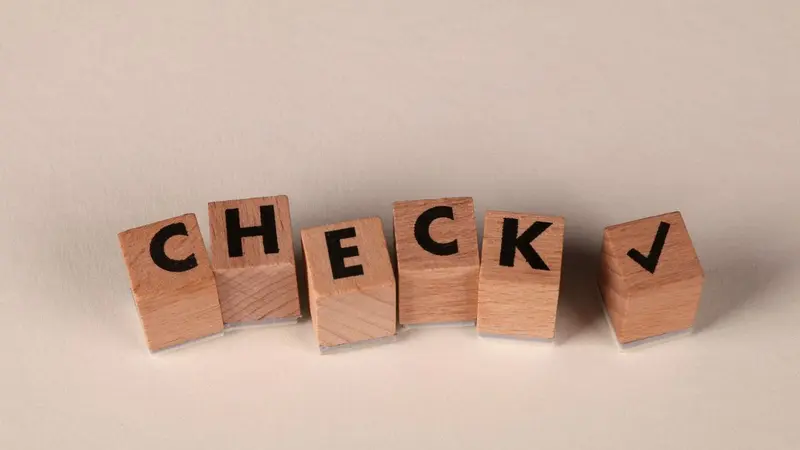 Wooden letter blocks spelling CHECK with a tick mark