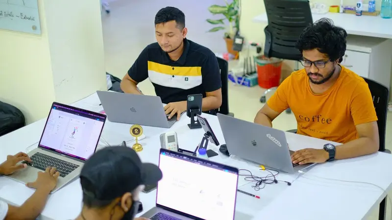 Team working at laptops around a shared desk in an office