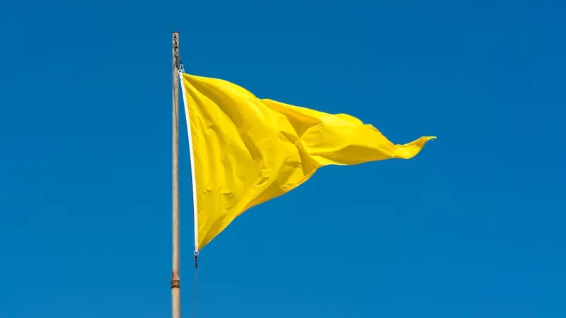 Yellow warning flag on a pole against a blue sky