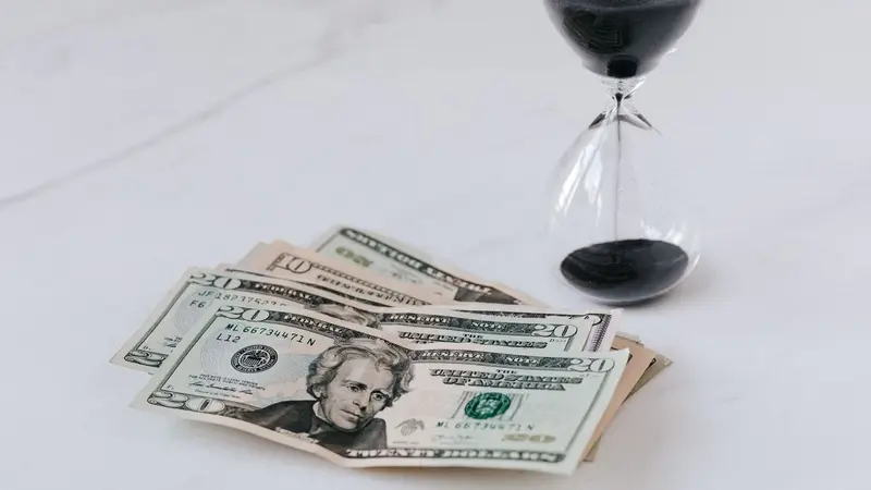Hourglass beside a stack of dollar bills, representing the cost of delay