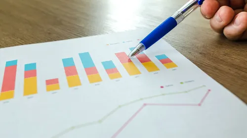 Printed bar chart with a hand holding a blue pen, analyzing growth results
