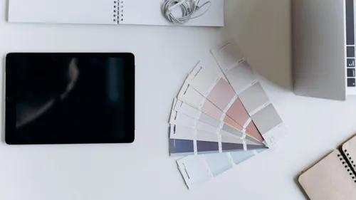 Tablet on a desk next to fabric color swatches and a notebook, representing design and color planning