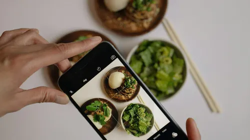 Hands holding a phone above a table to photograph bowls of healthy food