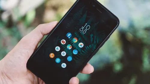 Hand holding a smartphone that displays a screen of mobile app icons