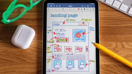 Tablet on a wooden desk showing a hand-drawn landing page wireframe