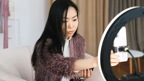 Woman adjusting a smartphone on a ring light stand to film content