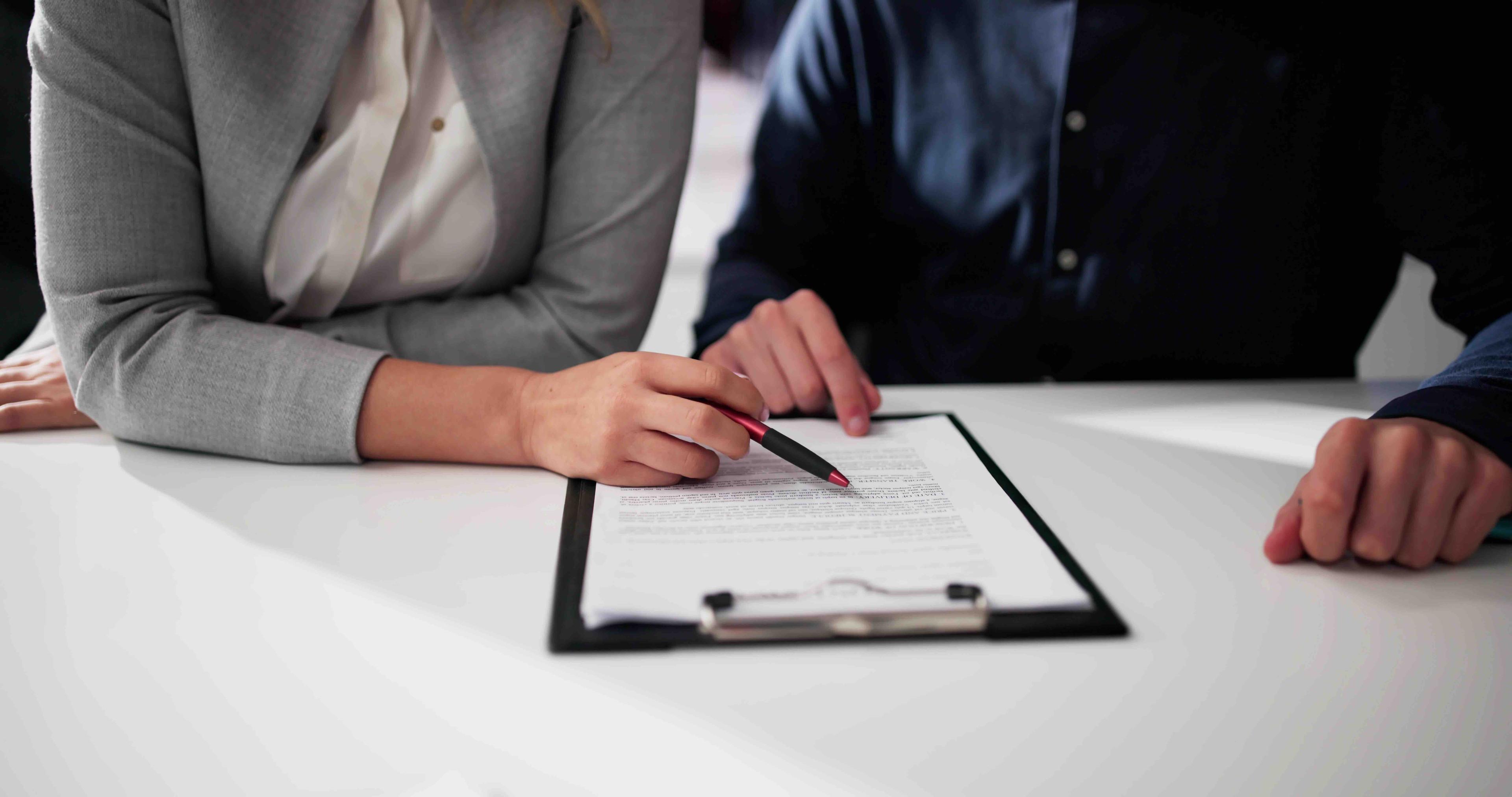Two people reviewing a document on a clipboard. One person points at the text with a pen.