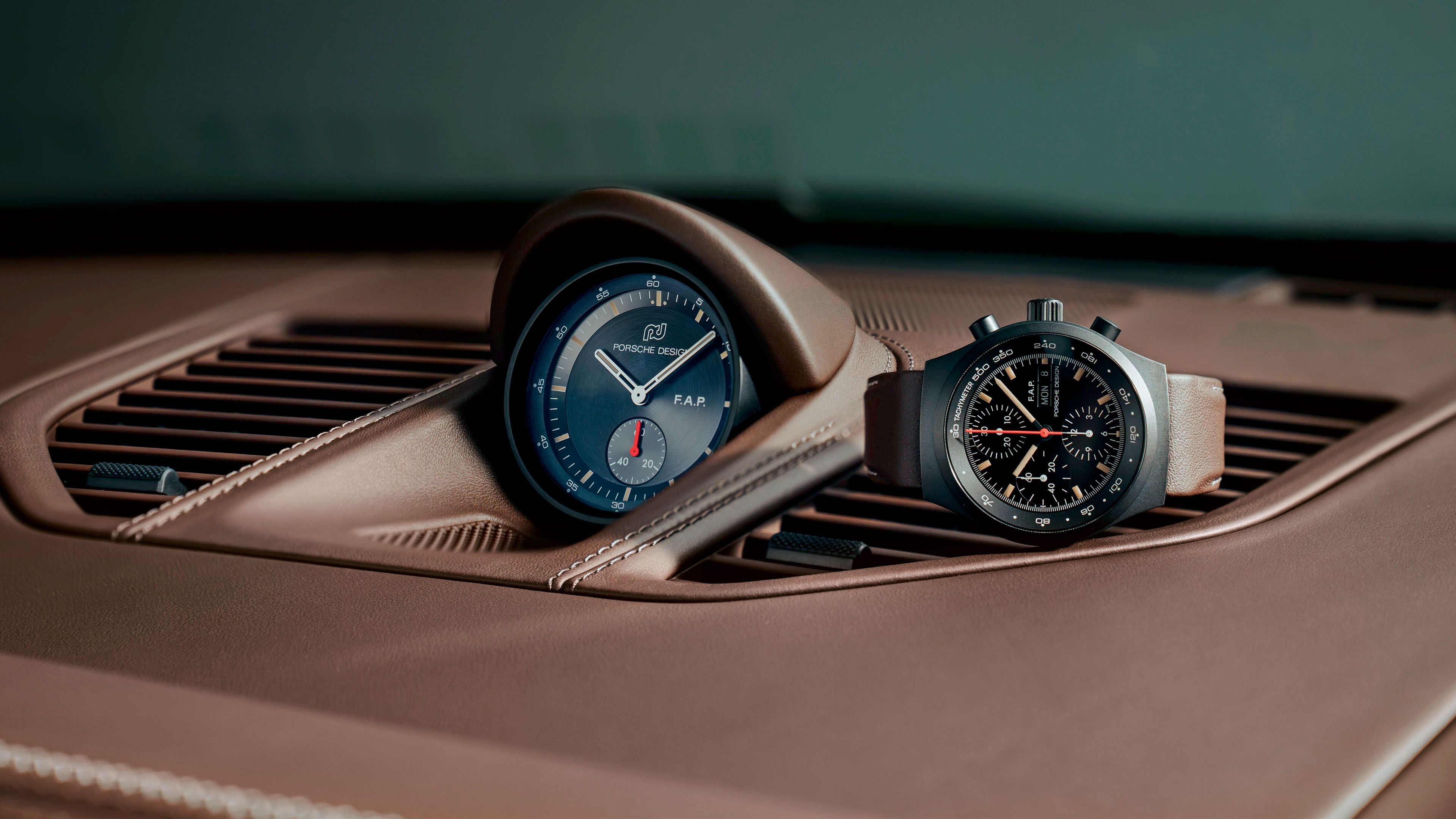 A Porsche Design Chronograph Watch and a dashboard clock, both resting on the brown leather interior of a car.