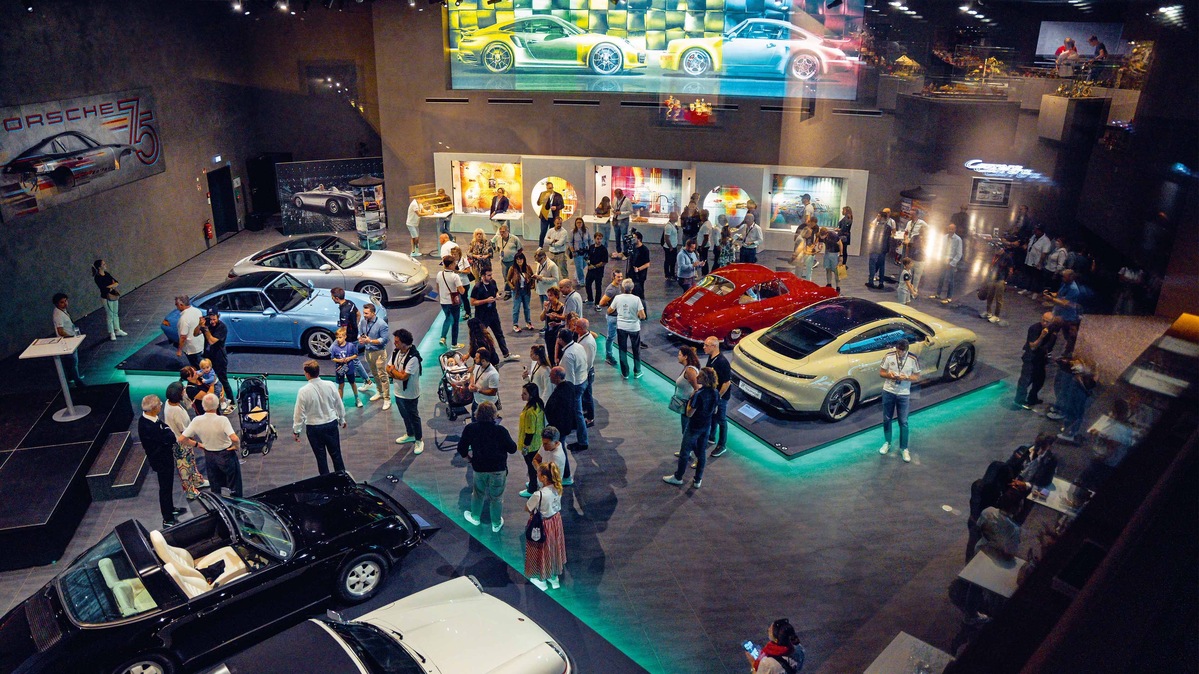 Visitors gather inside an exhibition hall surrounded by Porsche models from different eras.
