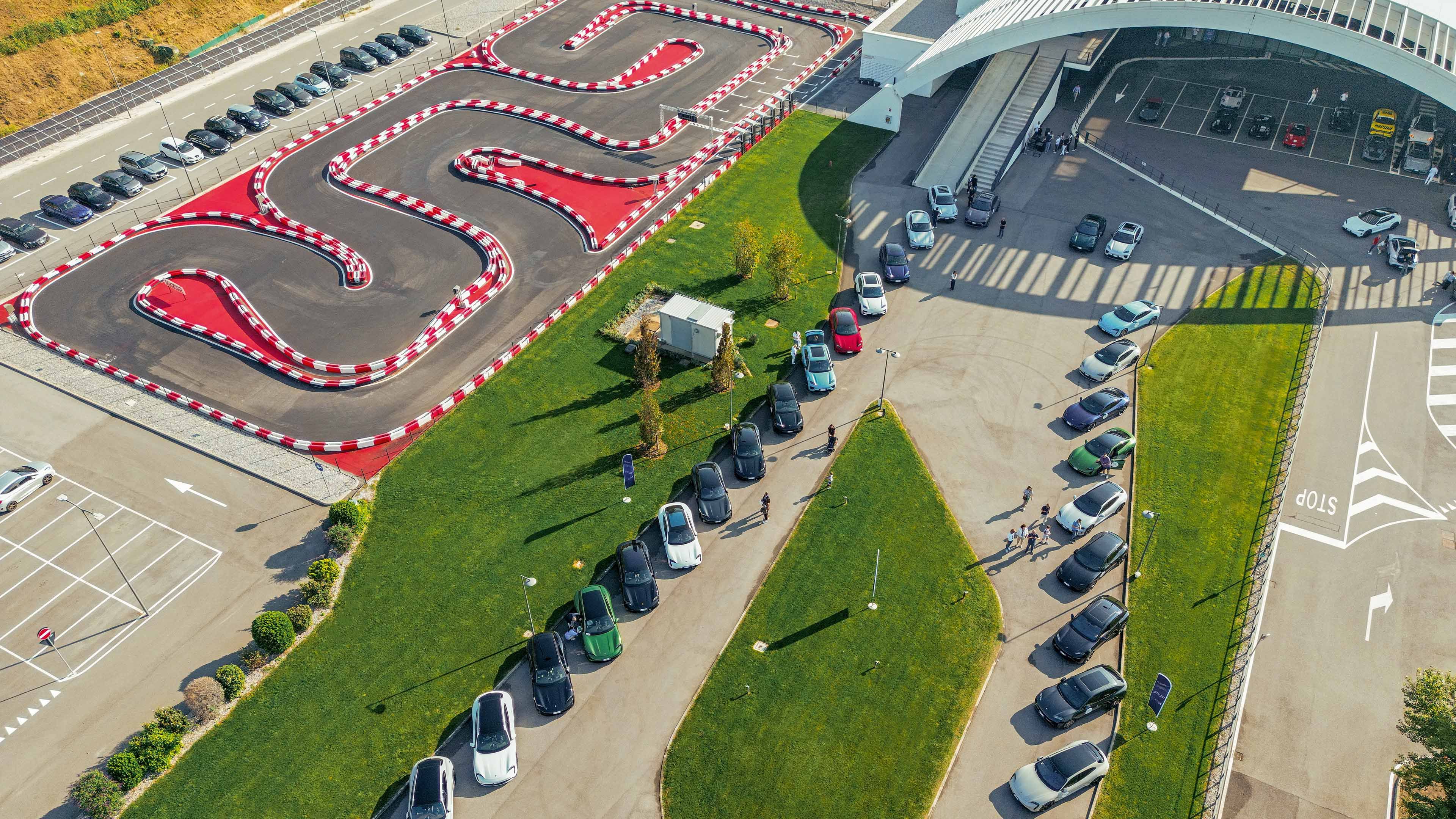 An aerial view shows a race track and long rows of parked vehicles next to an event building.