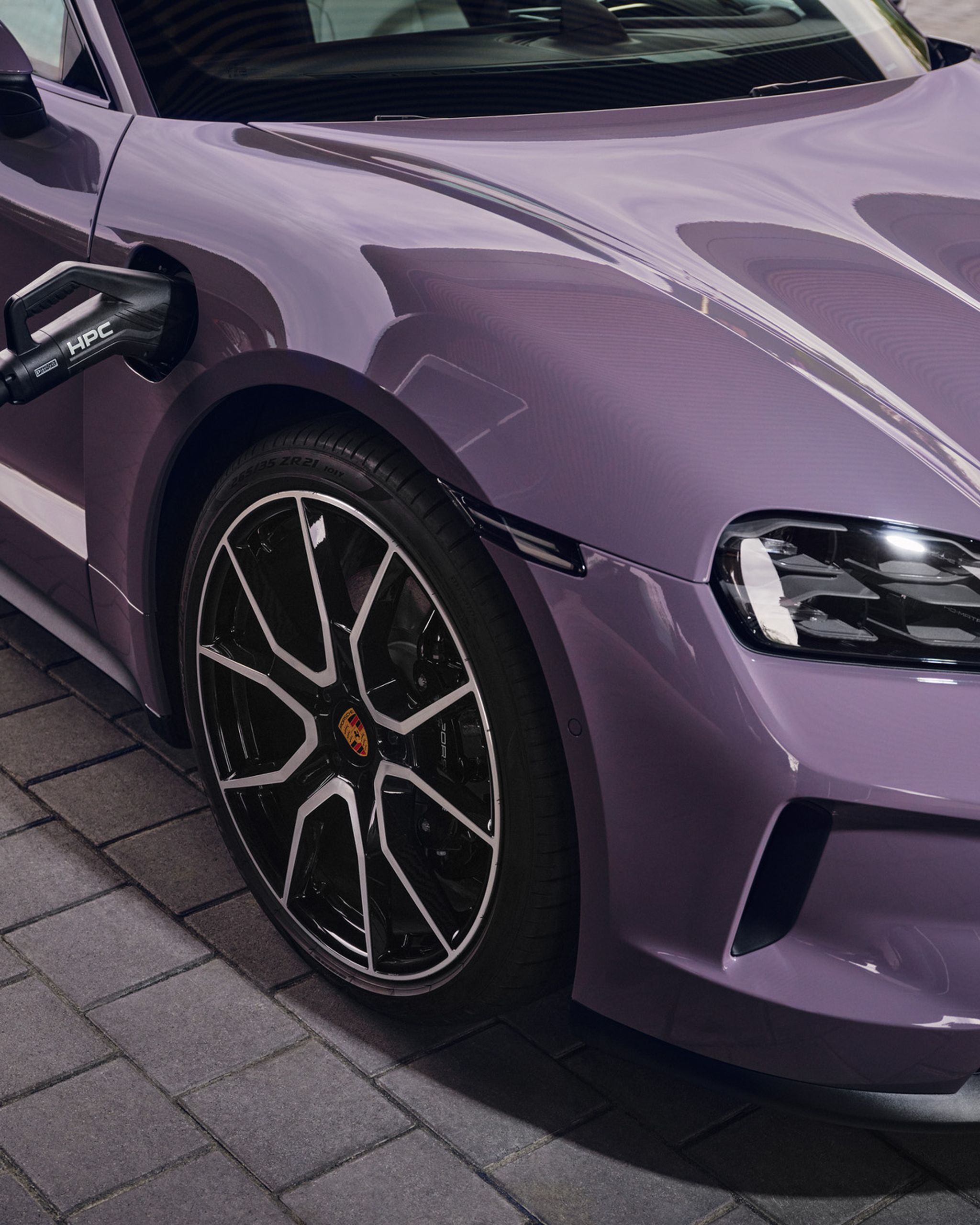 Purple electric car being charged, parked on a brick driveway. The charging cable is connected to the front left side of the vehicle.