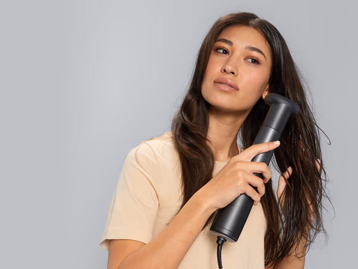 Woman styling wavy hair using Braun Air styler with thermal round brush attachment.