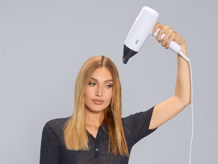 Woman drying straight blonde hair using Braun HD2.1 Hairdryer with drying nozzle.