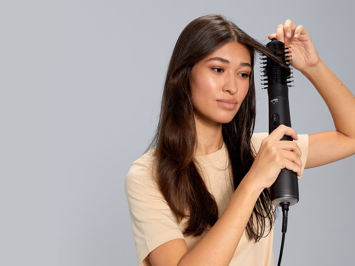 Model styling hair with dark grey Braun Air styler, creating soft waves.