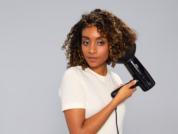 Woman with curly hair using Braun HD2.2 Hairdryer with diffuser attachment for volume and definition.