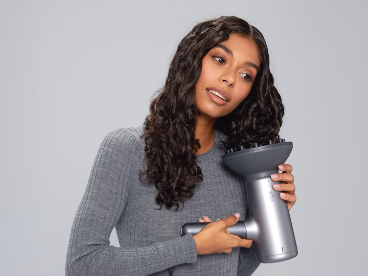 Woman styling curly hair with Braun HD 4.3 Hairdryer and diffuser attachment.