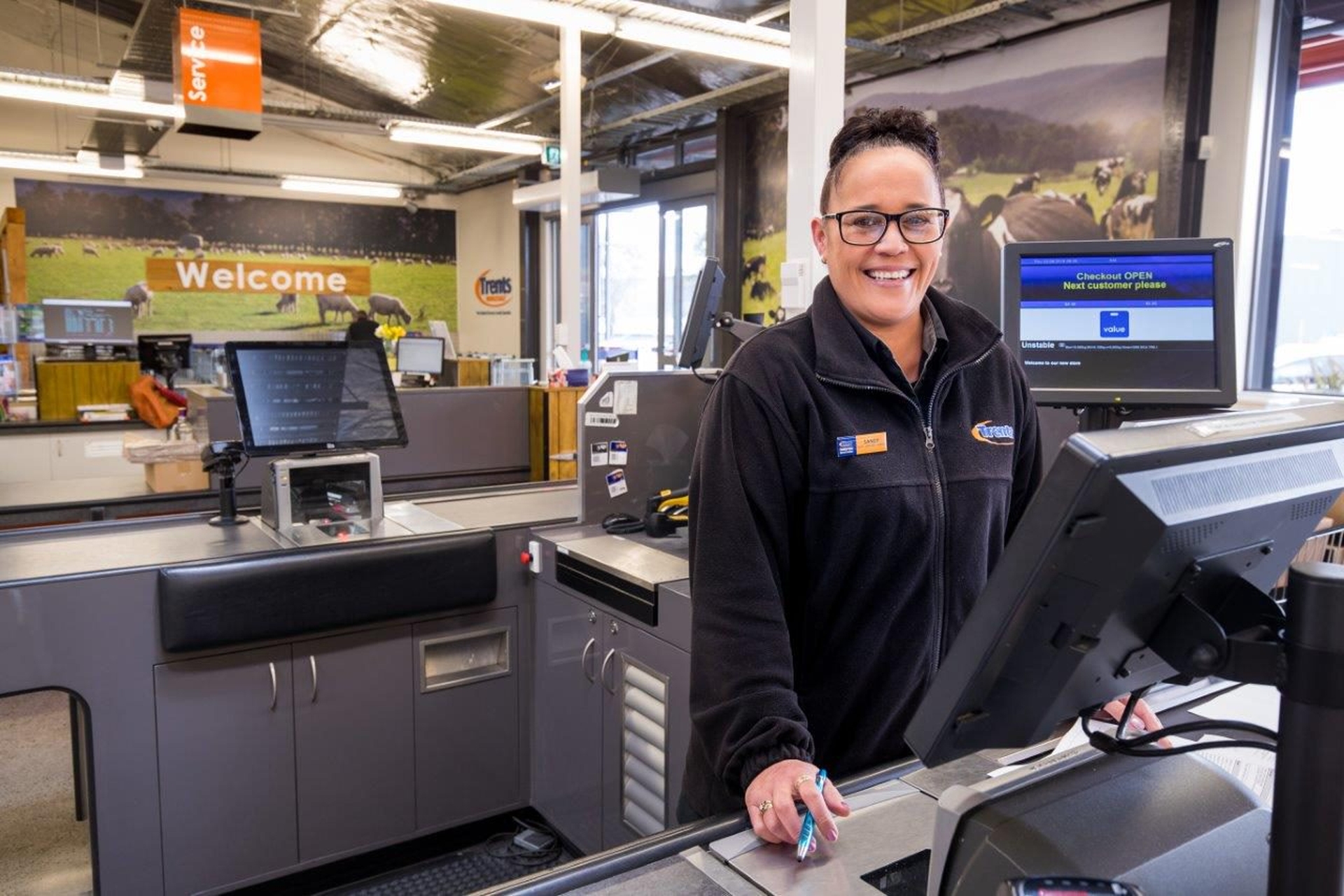 Smiling cashier standing behind a supermarket checkout counter with registers