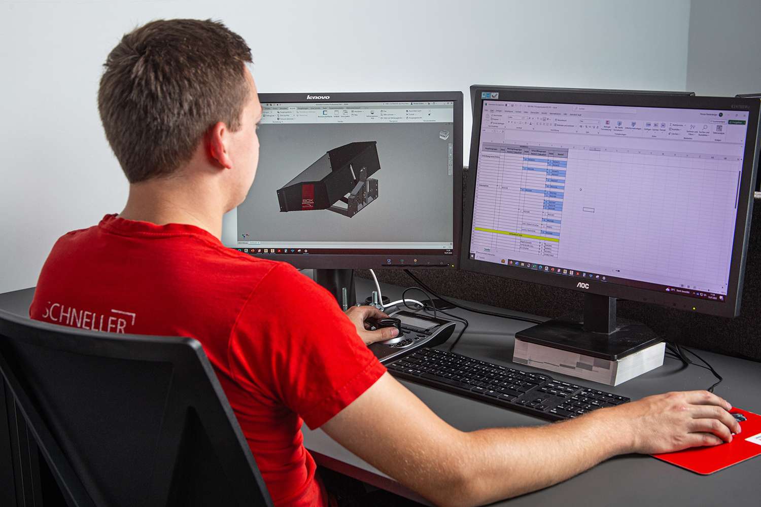 Person in a red shirt working at a desk with dual monitors displaying a 3D model and a spreadsheet.