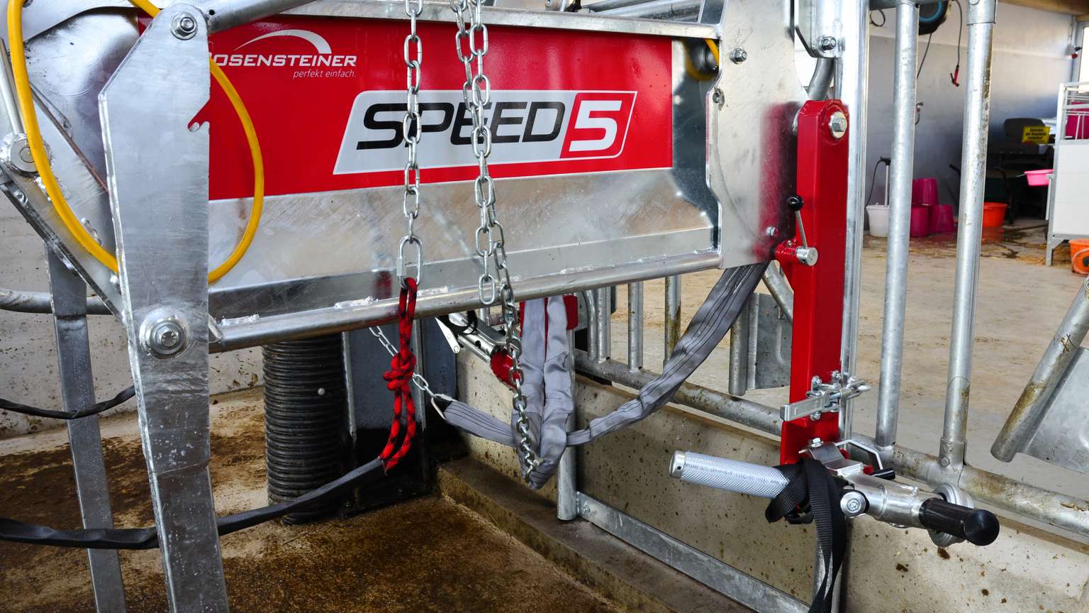 Close-up of a metal agricultural machine labeled "SPEED 5," with chains, levers, and a red panel in an industrial setting.