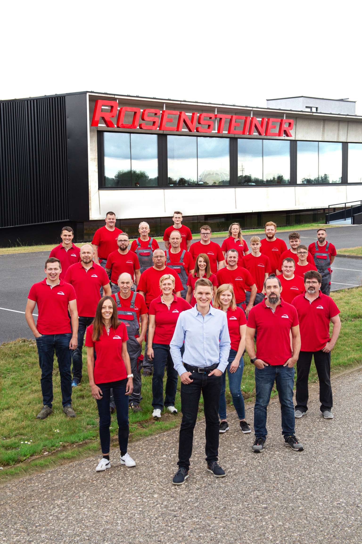 Mitarbeiterteam in Firmenkleidung und Geschäftsführer stehen lächelnd vor den Firmengebäude mit dem Schriftzug Rosensteiner.