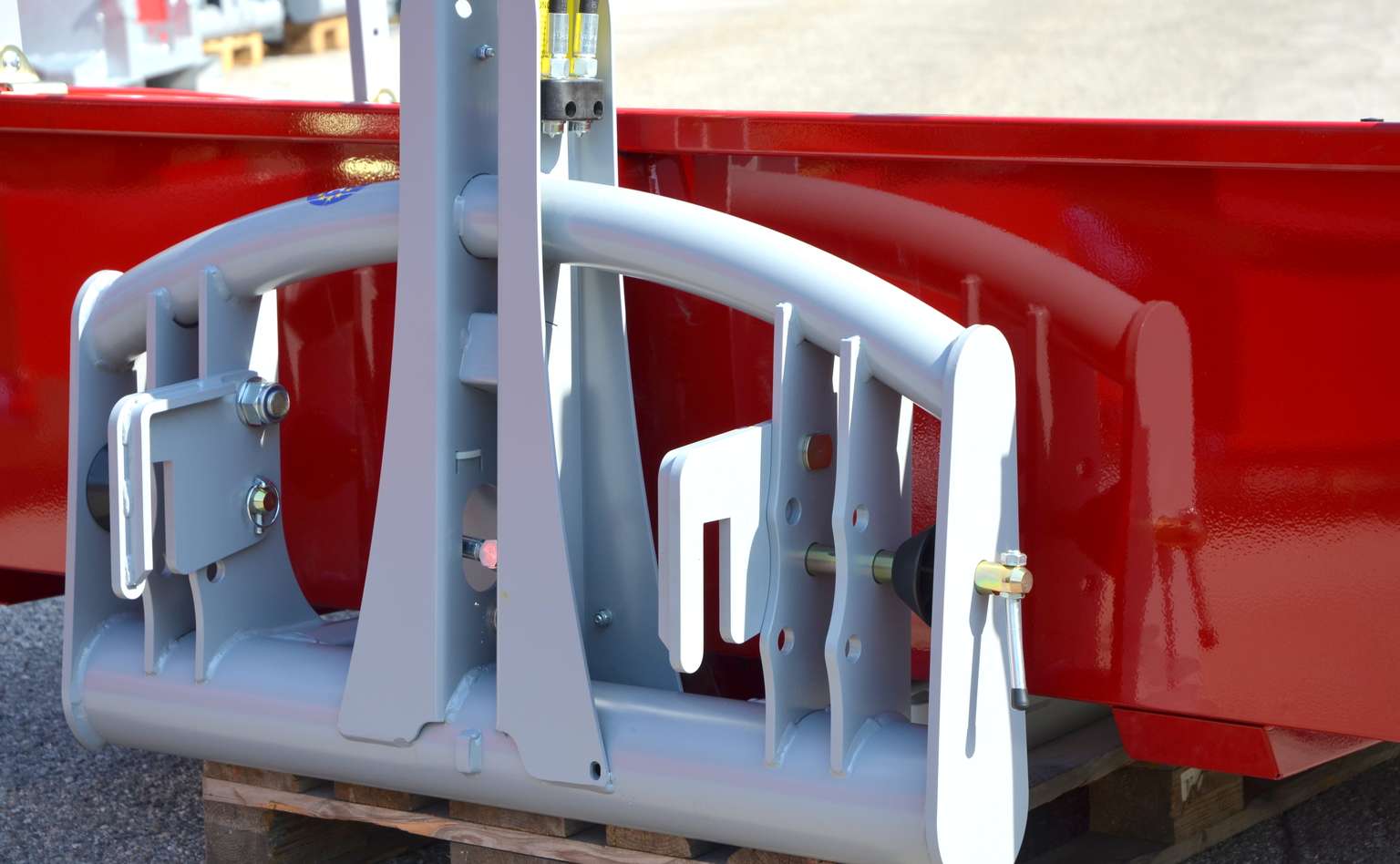 Close-up of a metal agricultural implement with a gray and red frame, displayed on a wooden pallet outdoors.