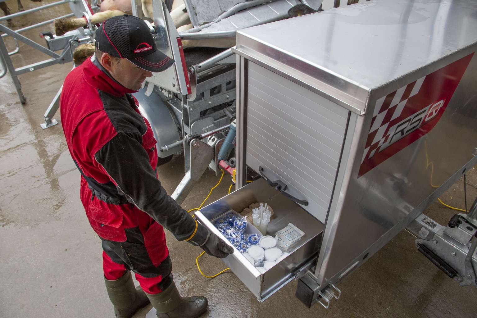 Person in red and black attire opens a drawer in a metallic cabinet, revealing various supplies, in an industrial setting.