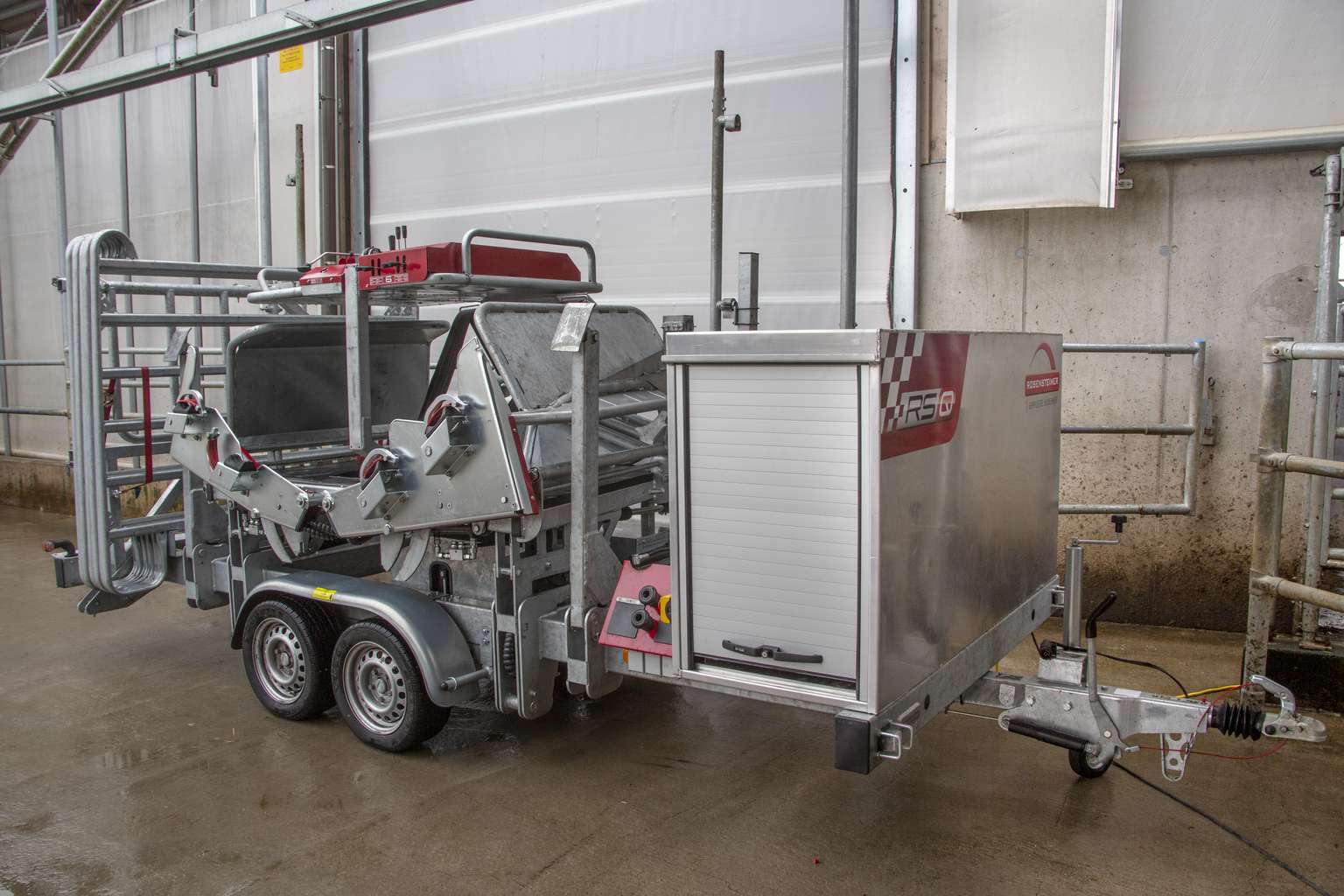 Mobile livestock handling and weighing system on a trailer, featuring metal structures and a control unit, parked in an industrial setting.