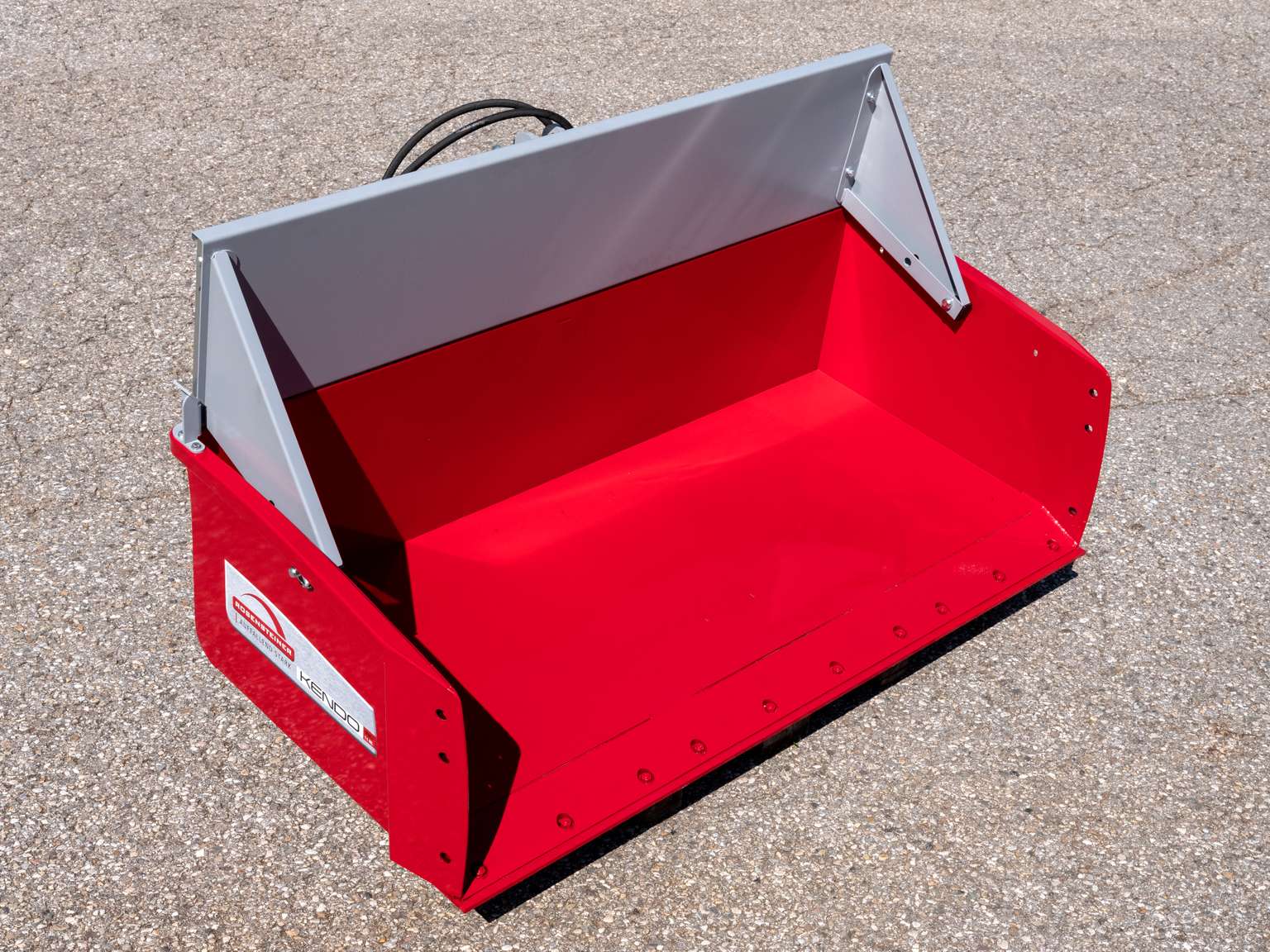 Red industrial snow pusher with a silver handle on a paved surface, designed for efficient snow removal.