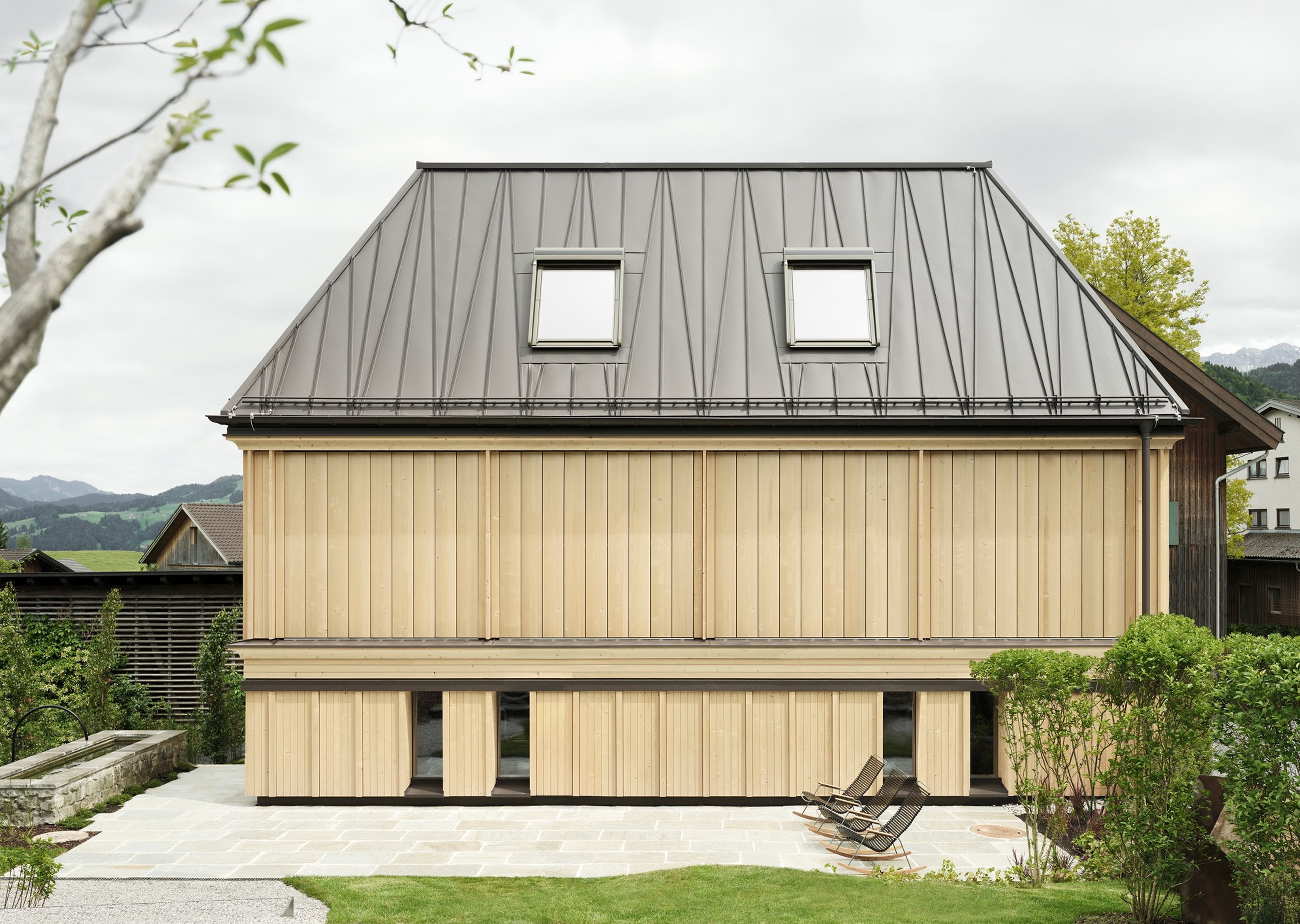Badehaus des Hotel Hirschen in Schwarzenberg: helles Holzgebäude mit dunklem Dach und Außenpool in einem Garten, Teil des Spa-Bereichs des Hotels.