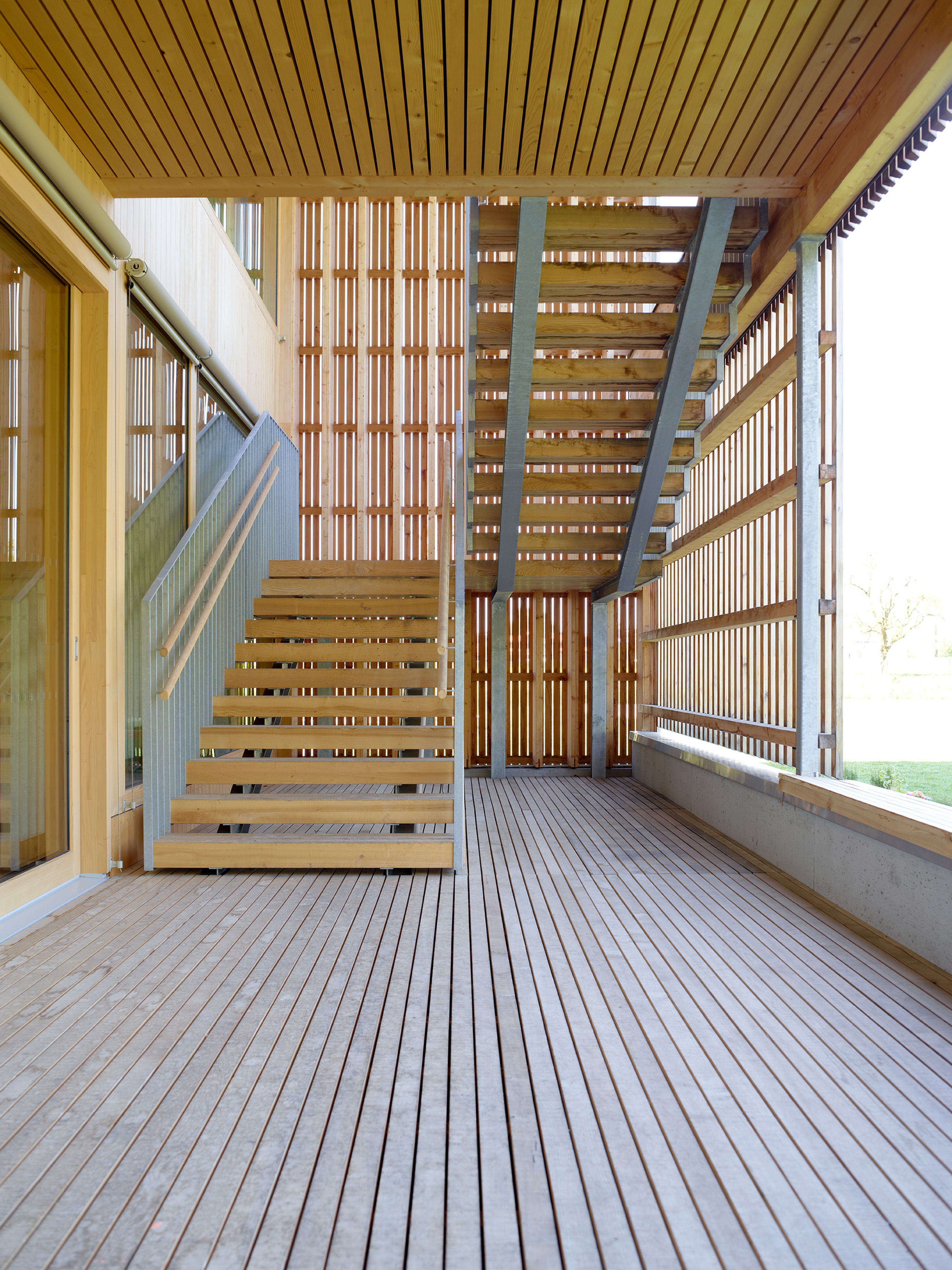 Außenaufnahme der Holzstiege eines Kindergartens in moderner Holzbauweise, mit sichtbarer Holzdecke und Außendiele aus Holz.