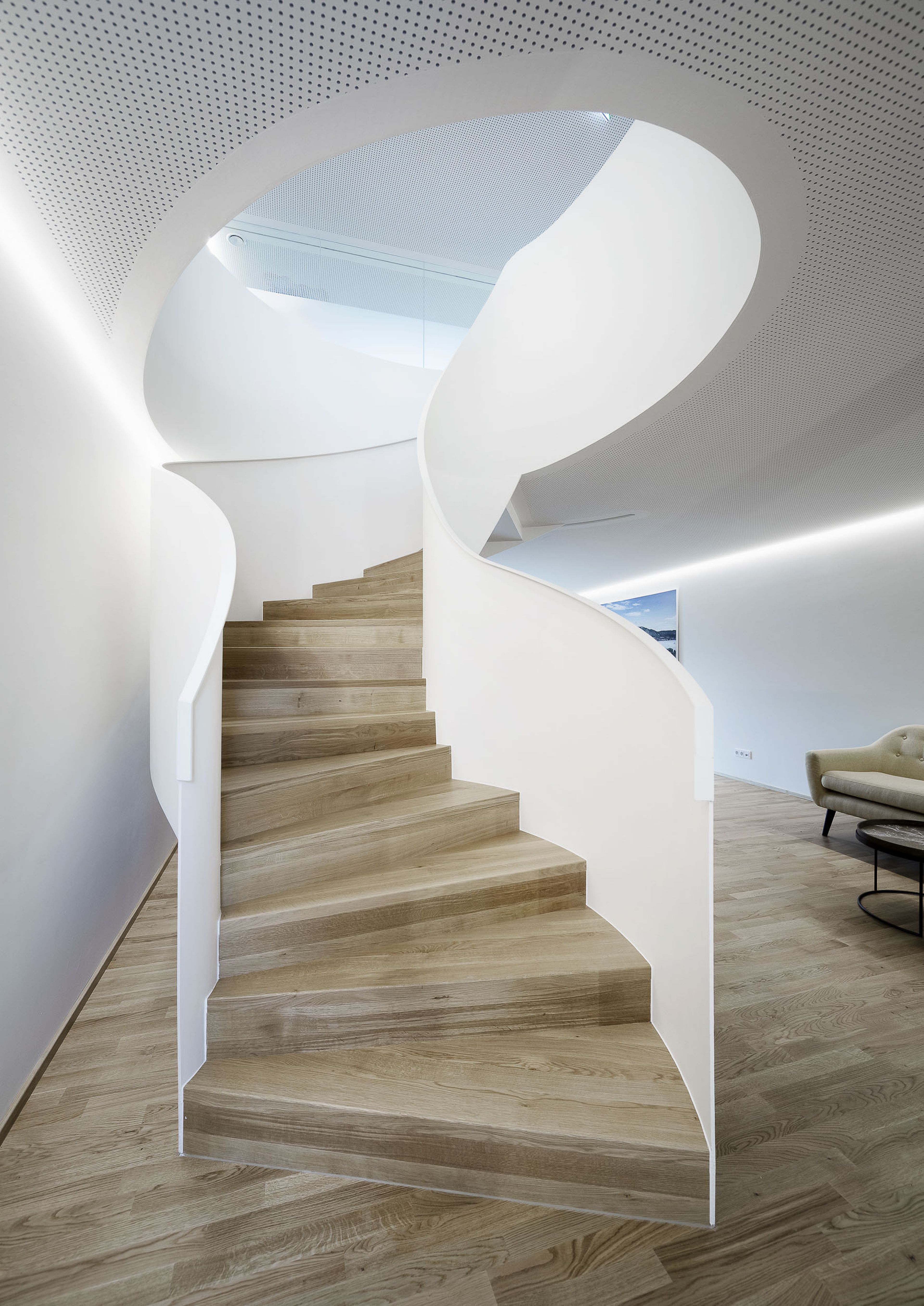 Moderne Wendeltreppe mit Holzstufen und eleganten weißen Wänden in einem minimalistischen Interieur mit hellem Holzboden.