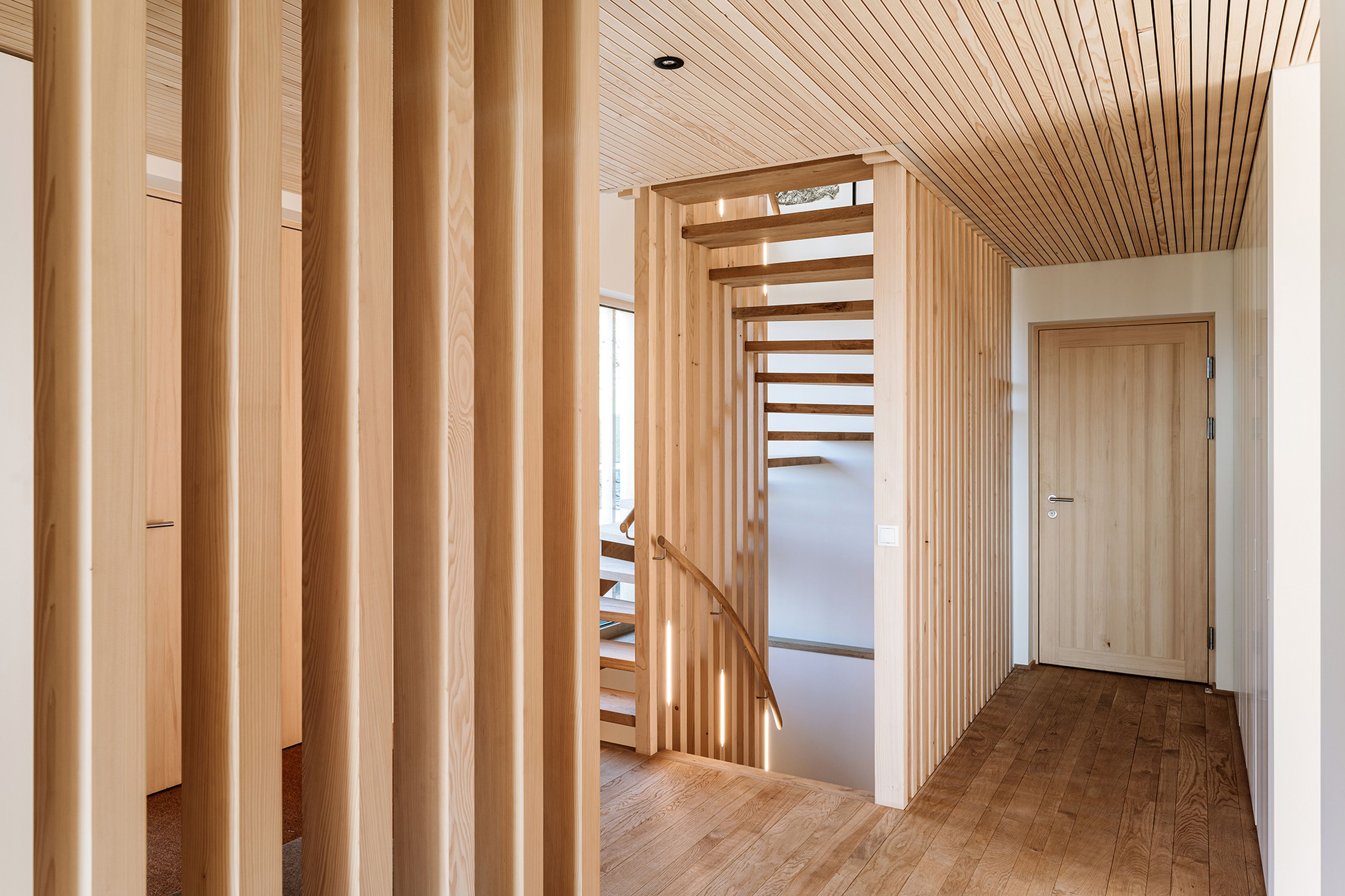 Modernes Interieur mit Holzlatten, Treppe und Holzboden. Helles Tageslicht unterstreicht das minimalistische, warme Design.