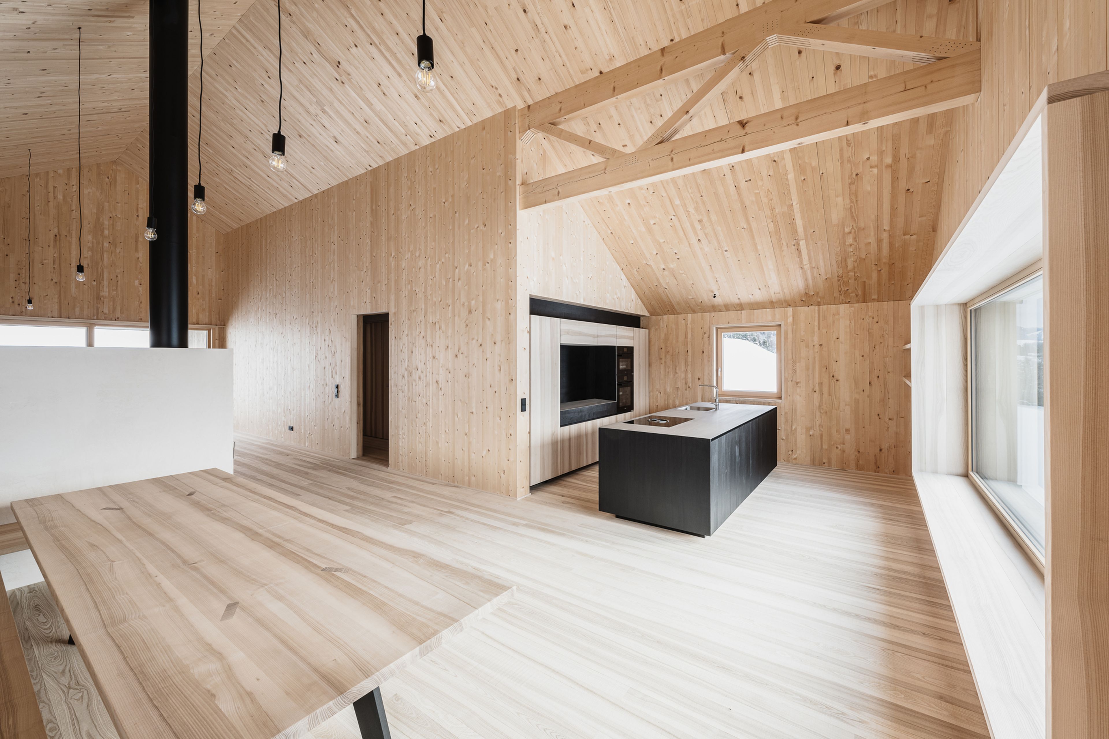 Modernes Interieur mit hellen Holzwänden und -decke, einer zentralen Kücheninsel, großen Fenstern und einem eleganten Esstisch.