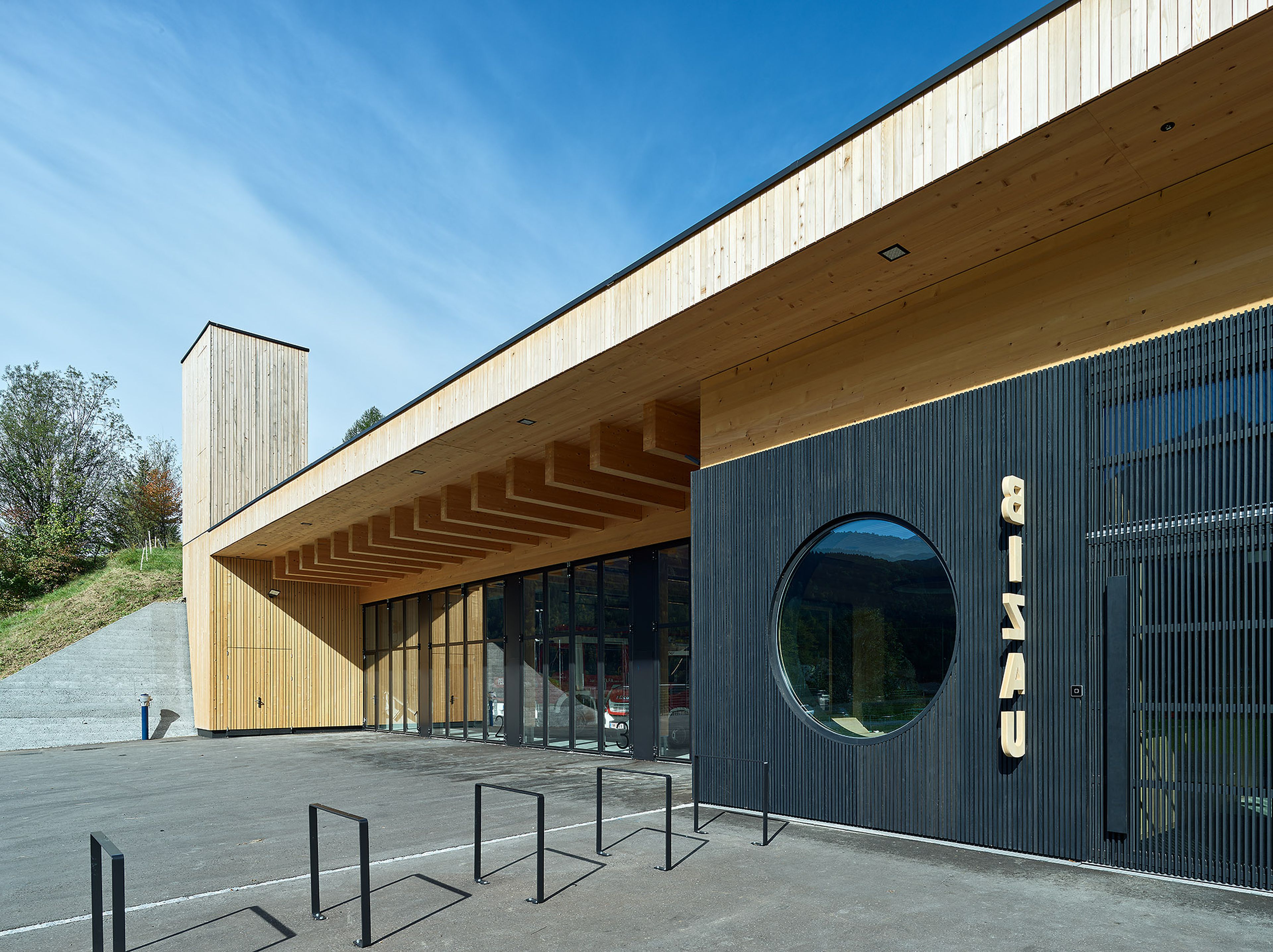 Modernes Gebäude mit Holzfassade, großen Glasfenstern und einem runden Fenster an einem bewölkten Tag, das sich durch ein schlichtes, elegantes Design auszeichnet.