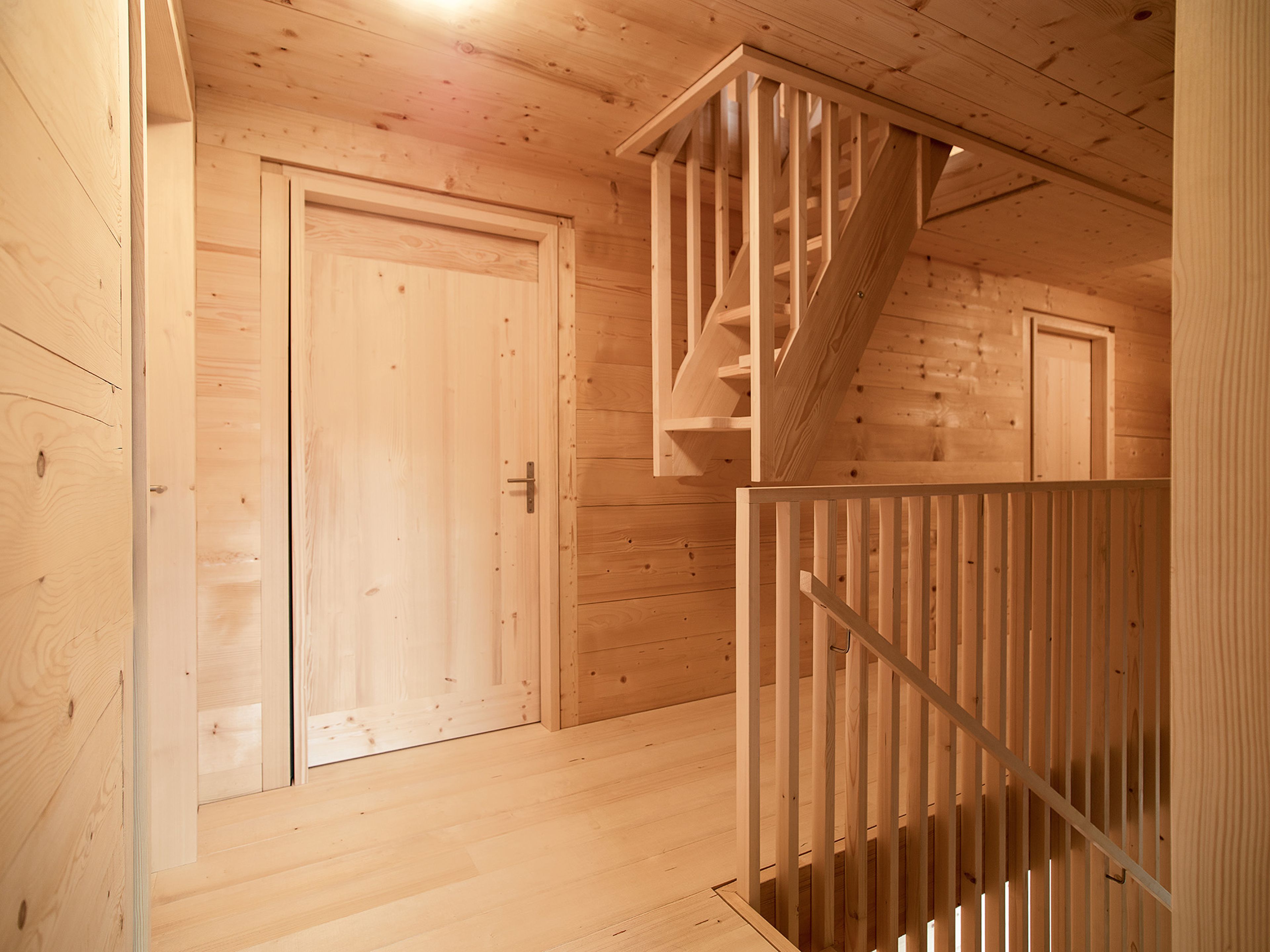 Holzvertäfeltes Interieur eines Hauses mit einem Flur mit zwei geschlossenen Türen und einer Treppe mit senkrechten Geländern, die zum Obergeschoss führt.