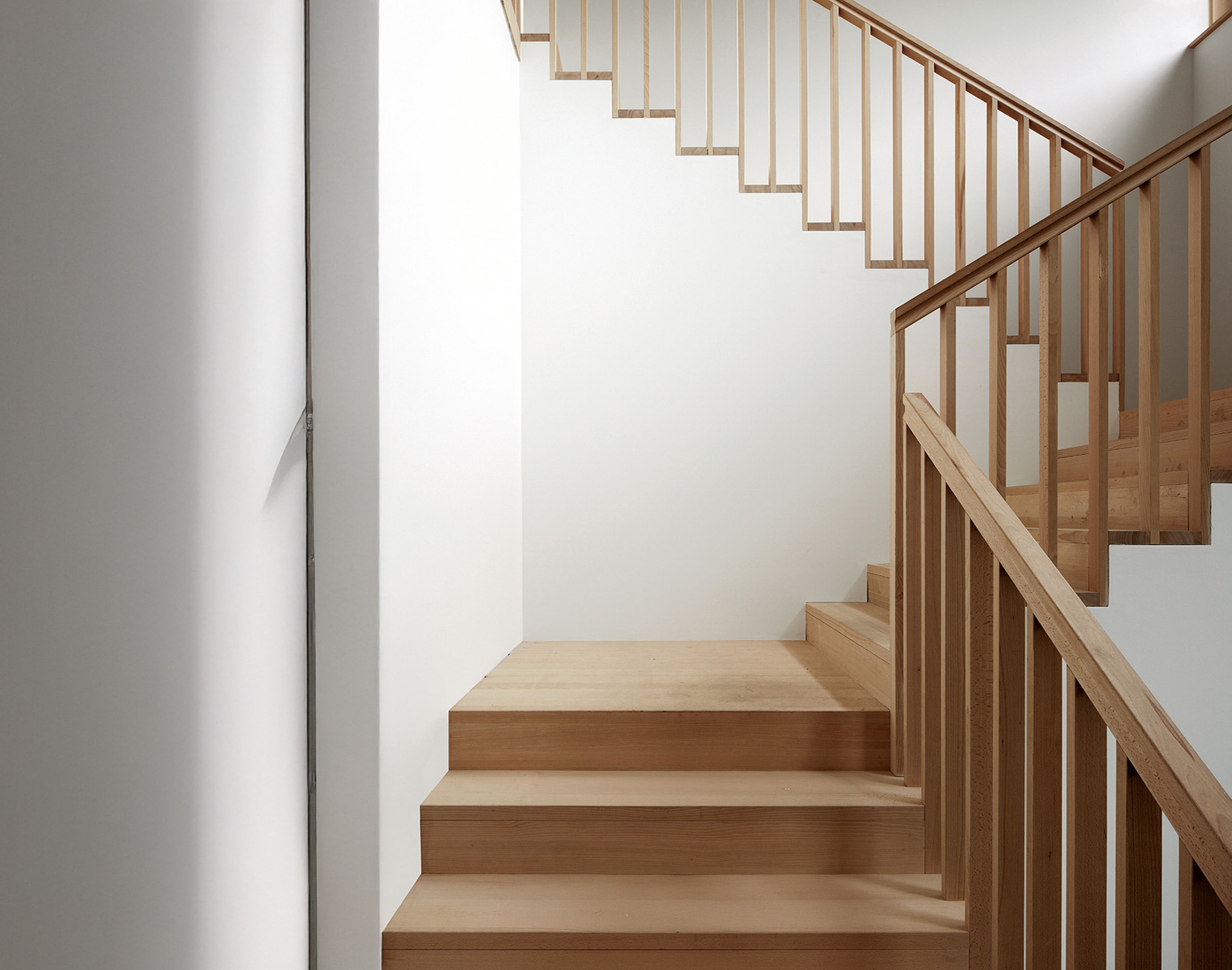 Minimalistische Holztreppe mit klaren Linien, weißen Wänden und natürlicher Oberfläche, die einen modernen und luftigen architektonischen Look erzeugt.