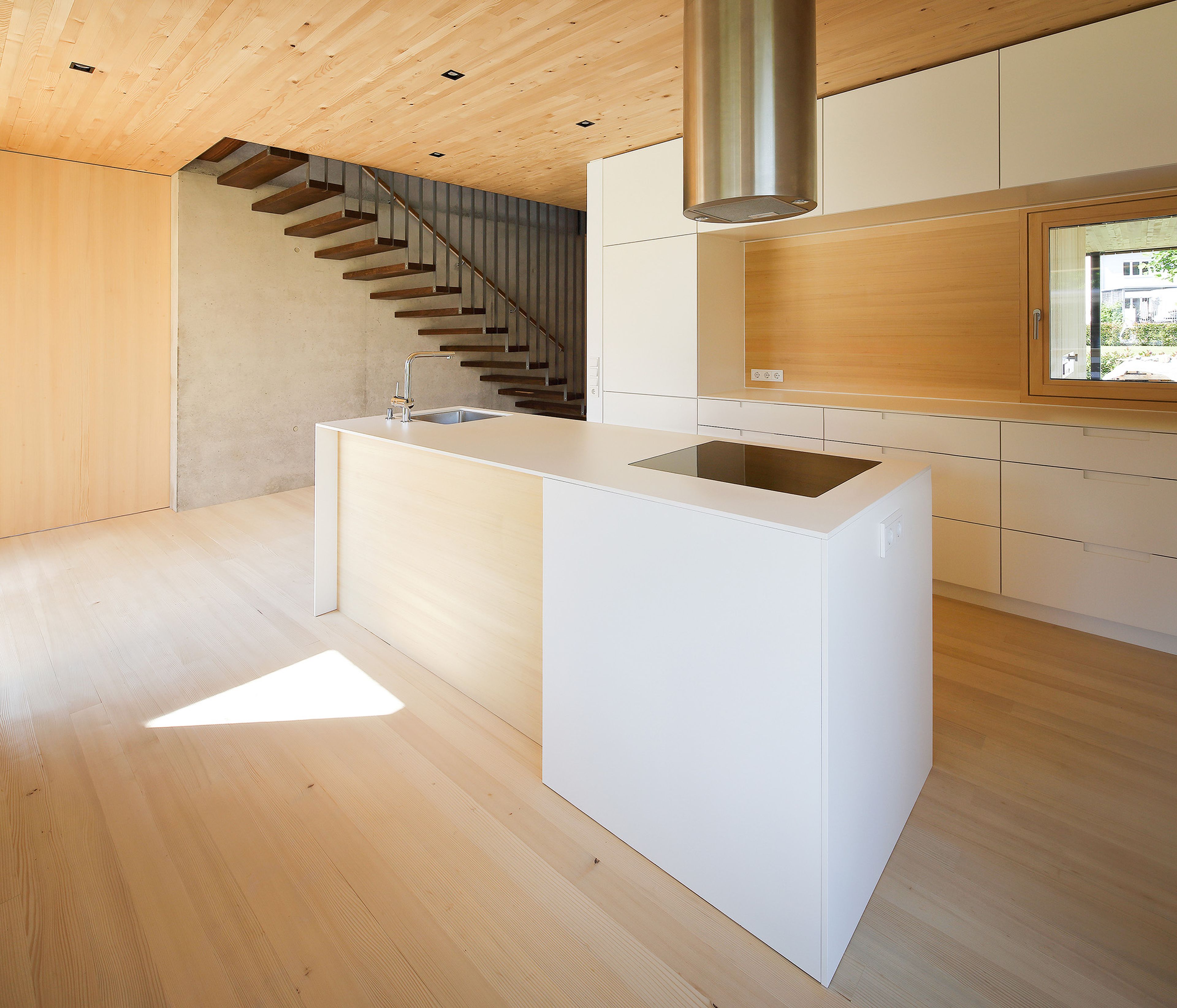 Innenansicht eines Holzhauses mit weißer, moderner Küche und offener Stiege mit Stahlgeländer, Holzdecke und Holzboden